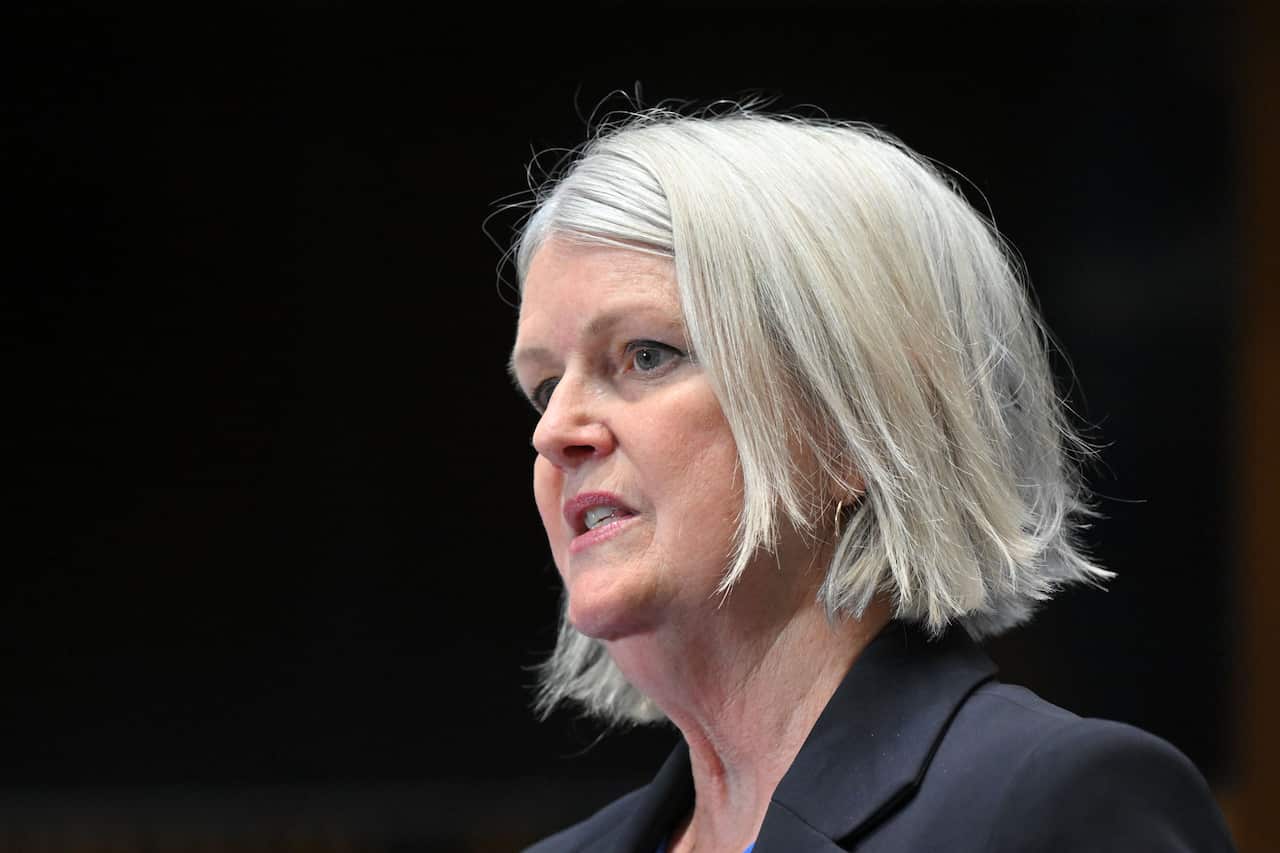 A woman with short hair, wearing a blazer, speaks.