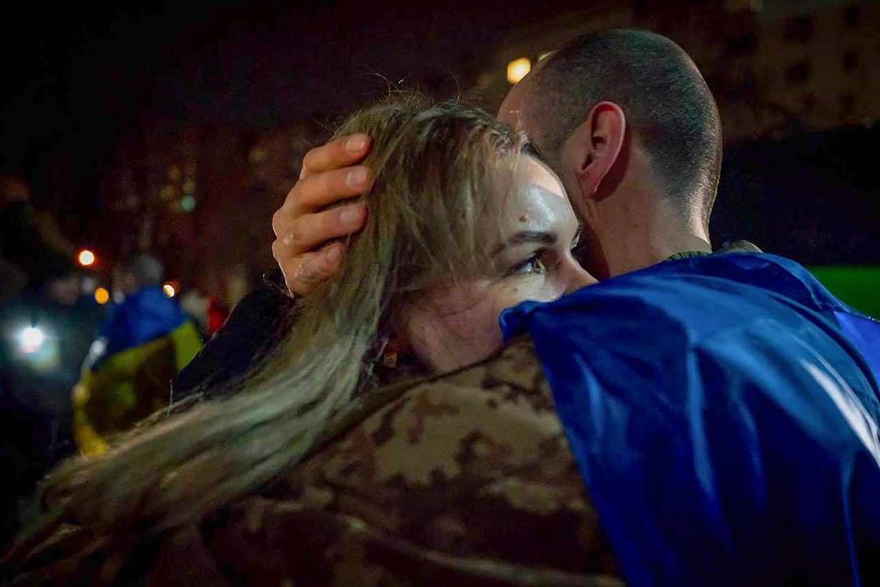 A man in military fatigue hugs a woman.