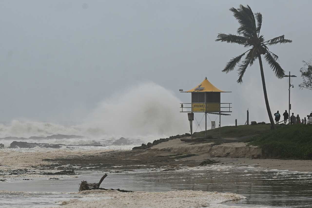 A large wave hits the shoreline behind a yellow lifeguard watchtower 