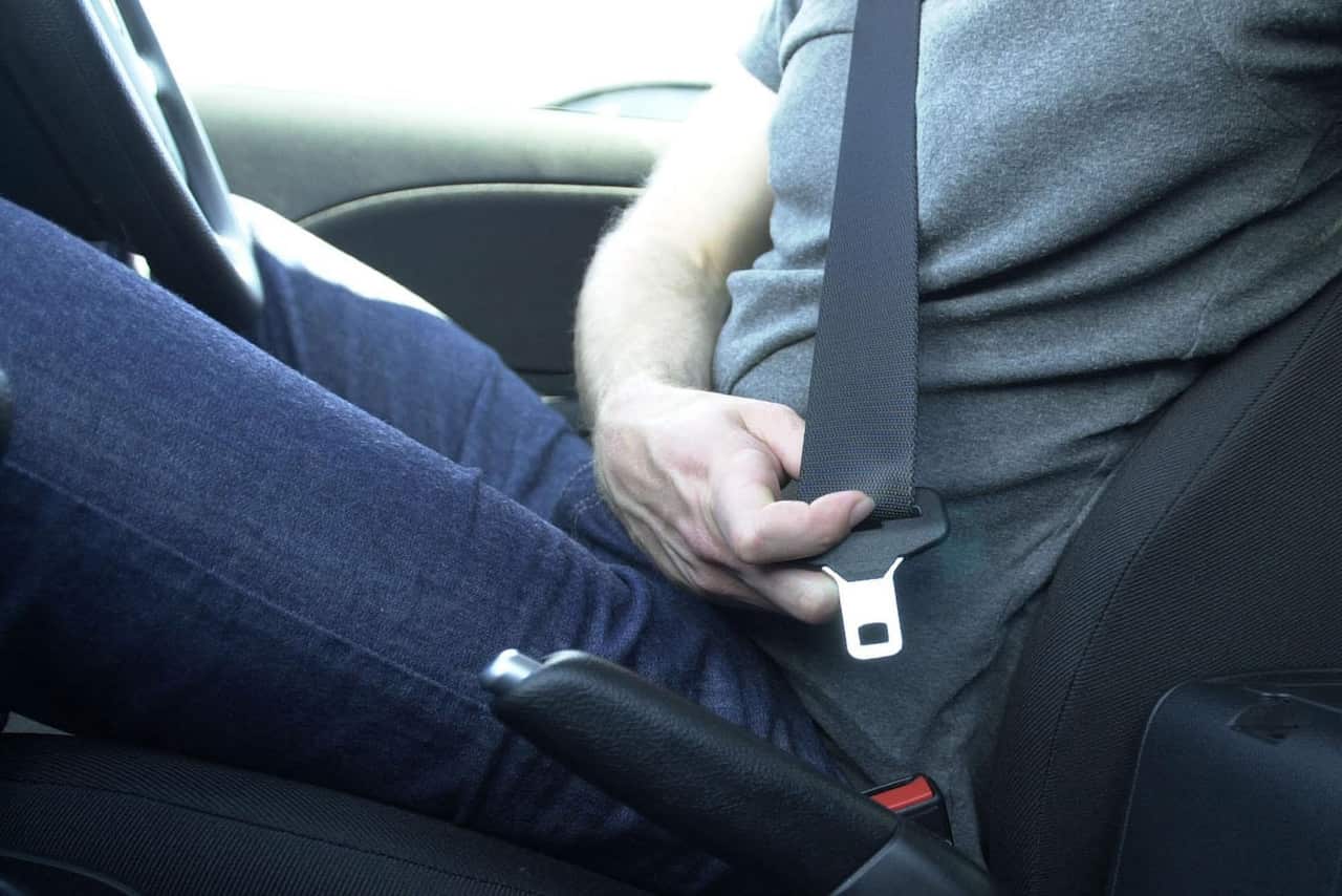 A man poulls a seatbelt across his lap and plugs it in.