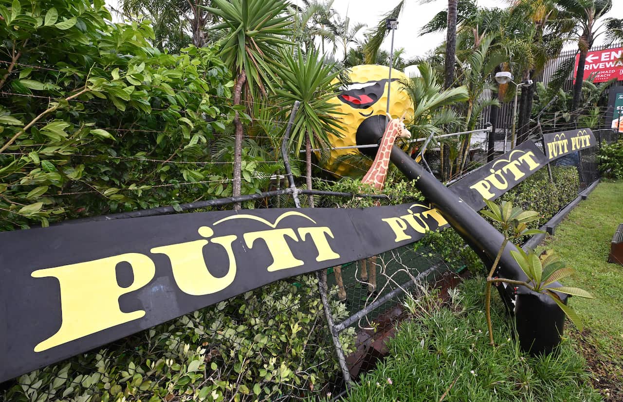 A damaged sign that reads "putt putt" with a street light fallen through it. 