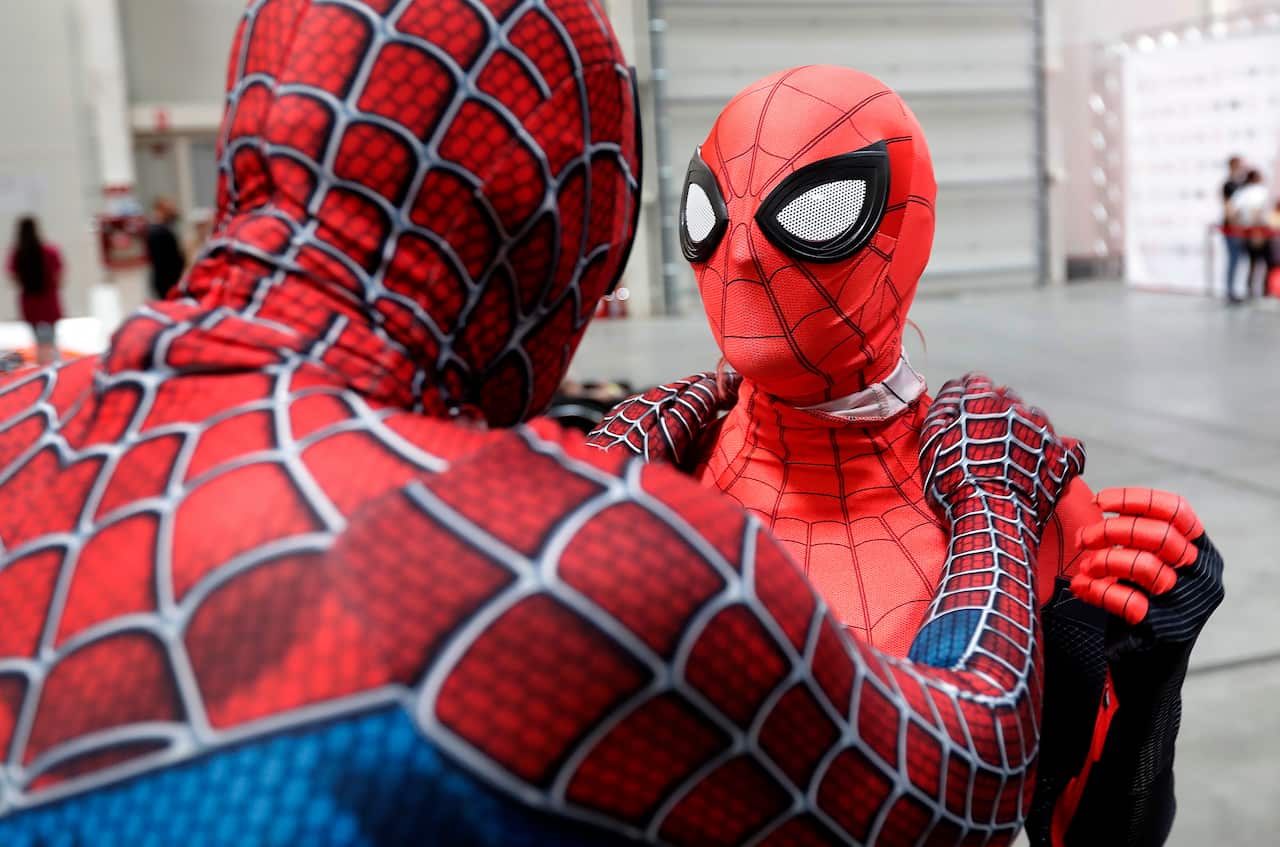 A Spiderman cosplayer helps another put her costume on at a Comic Con event.