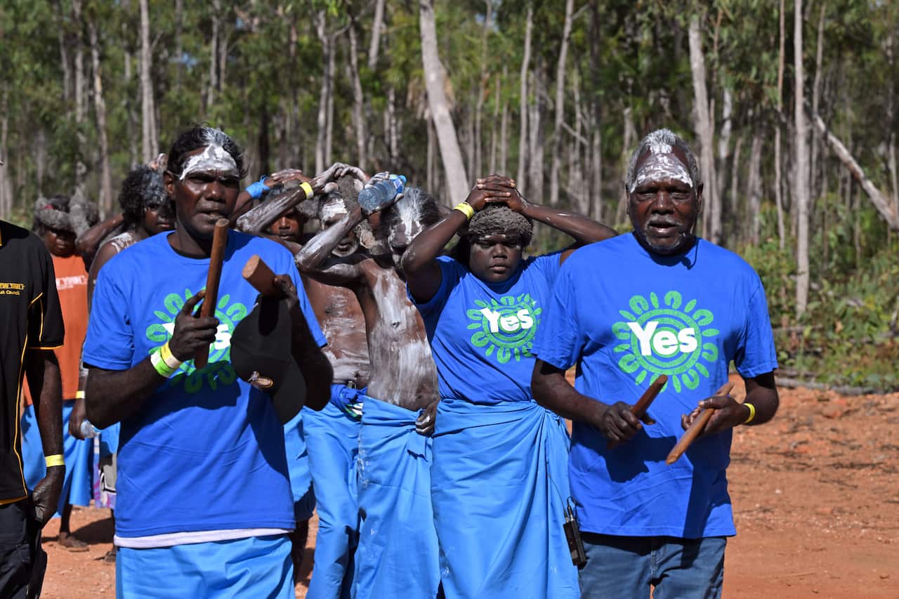 Members of the Yolngu people, some wearing blue T-shirts with "Yes" written on them, perform a ceremonial welcome.