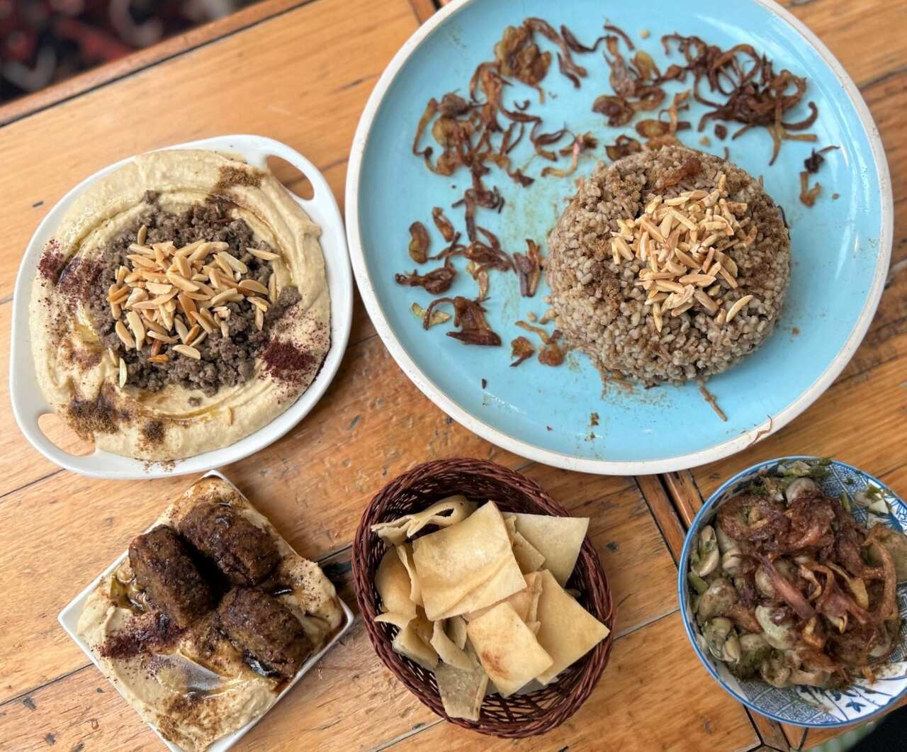 Plates of Middle Eastern food sit on a wooden table.