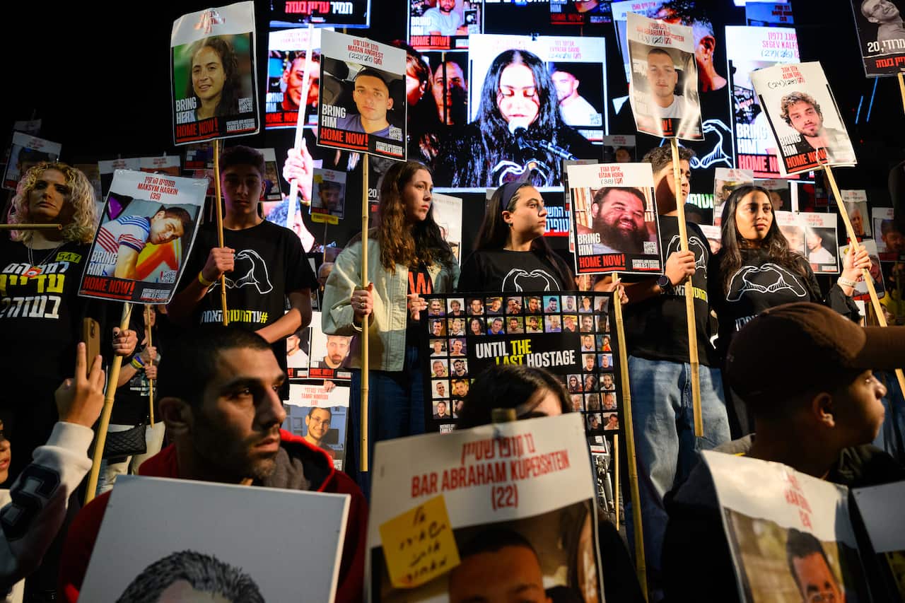 A group of protesters gather, holding signs with images of Israeli hostages. 