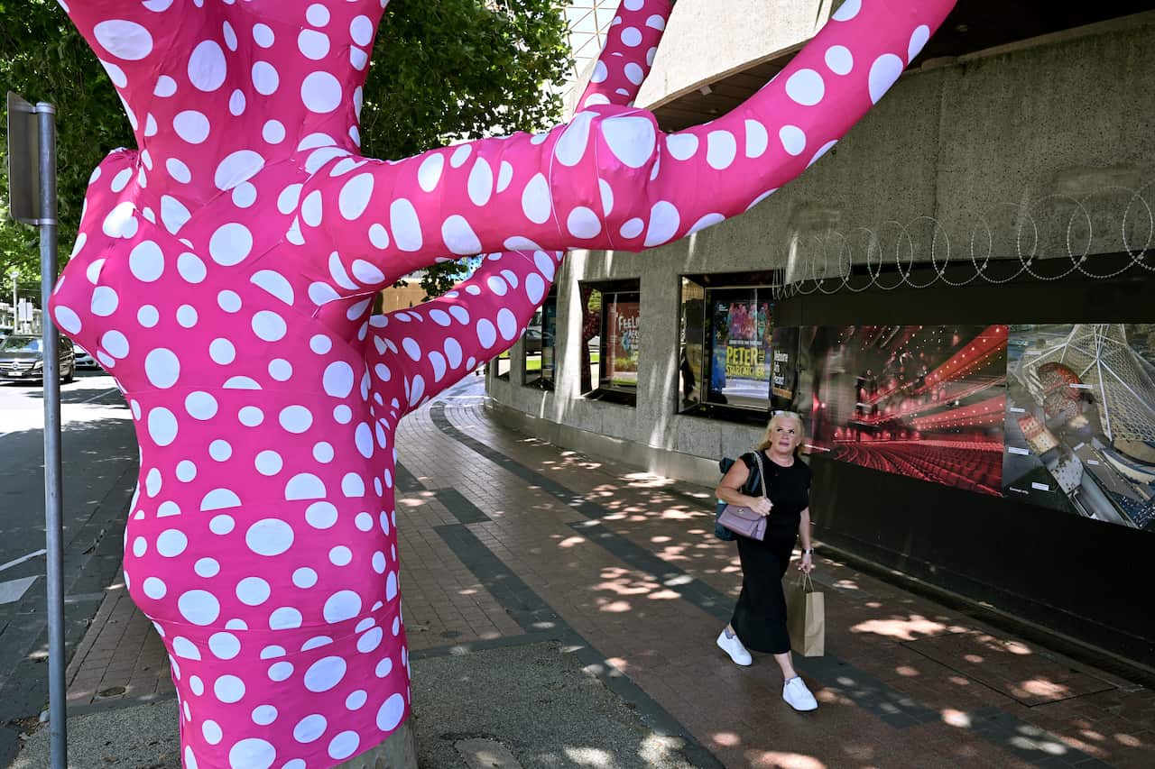 A woman looks at a tree covered in pink wrap with white polka dots