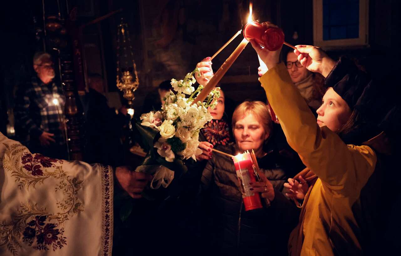 Several people light candles from one being held out by a priest in a darkened church.