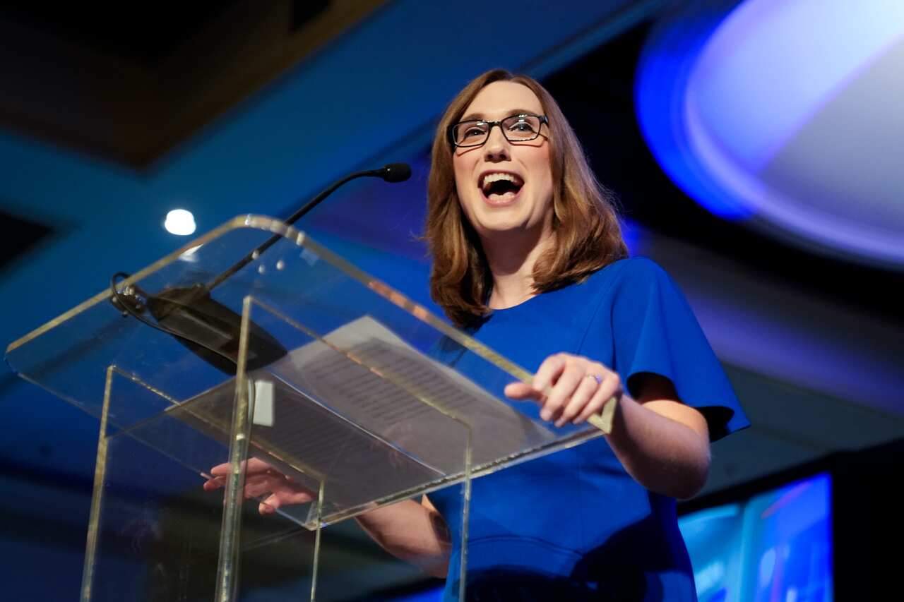 A woman wearing a blue dress speaks at a podium. 