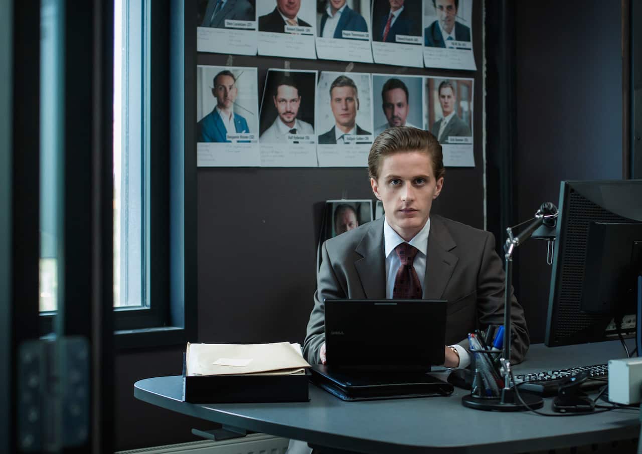A man wearing a suit sits in an office in front of a computer.jpg