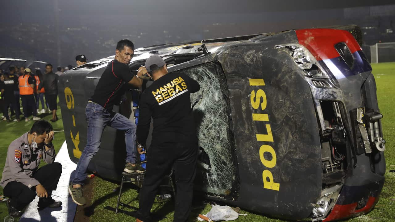 People climb on a damaged police car during a riot at a football stadium