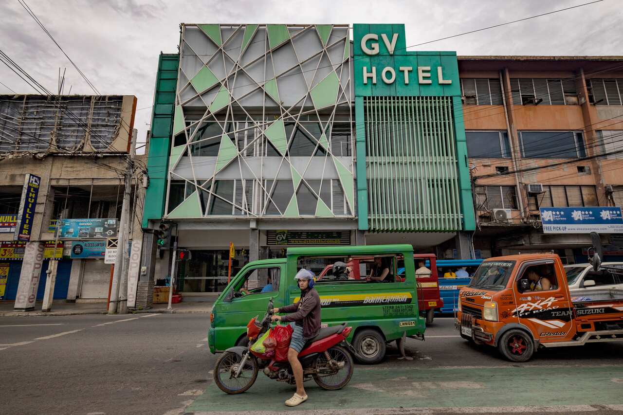 Small trucks on a street in front of a smallish building with green and white frontage and a sign GV Hotel