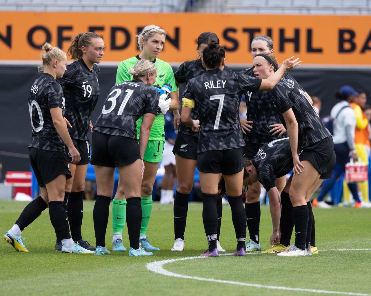 Women footballers wearing black uniforms stand together on a pitch