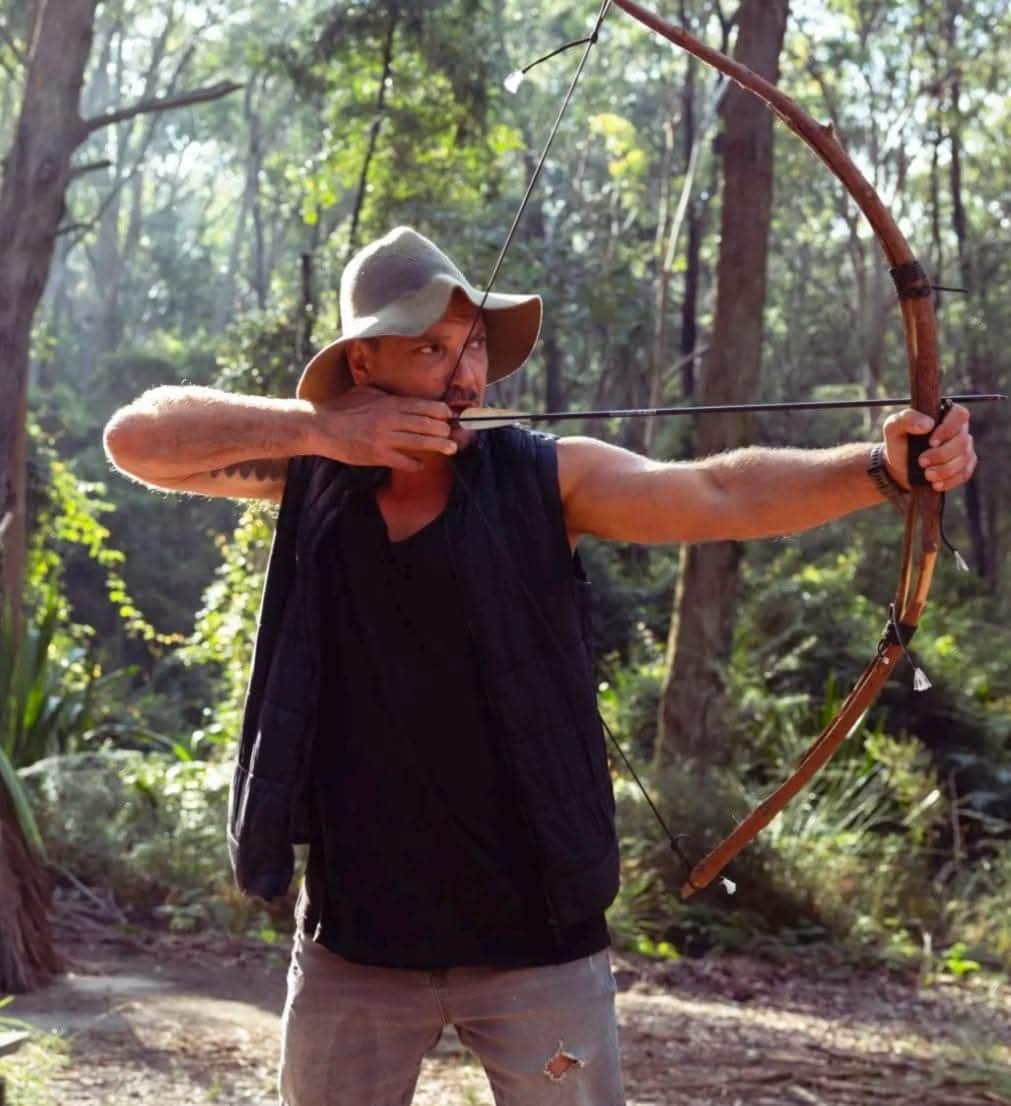 A man holding a crossbow in the bush.