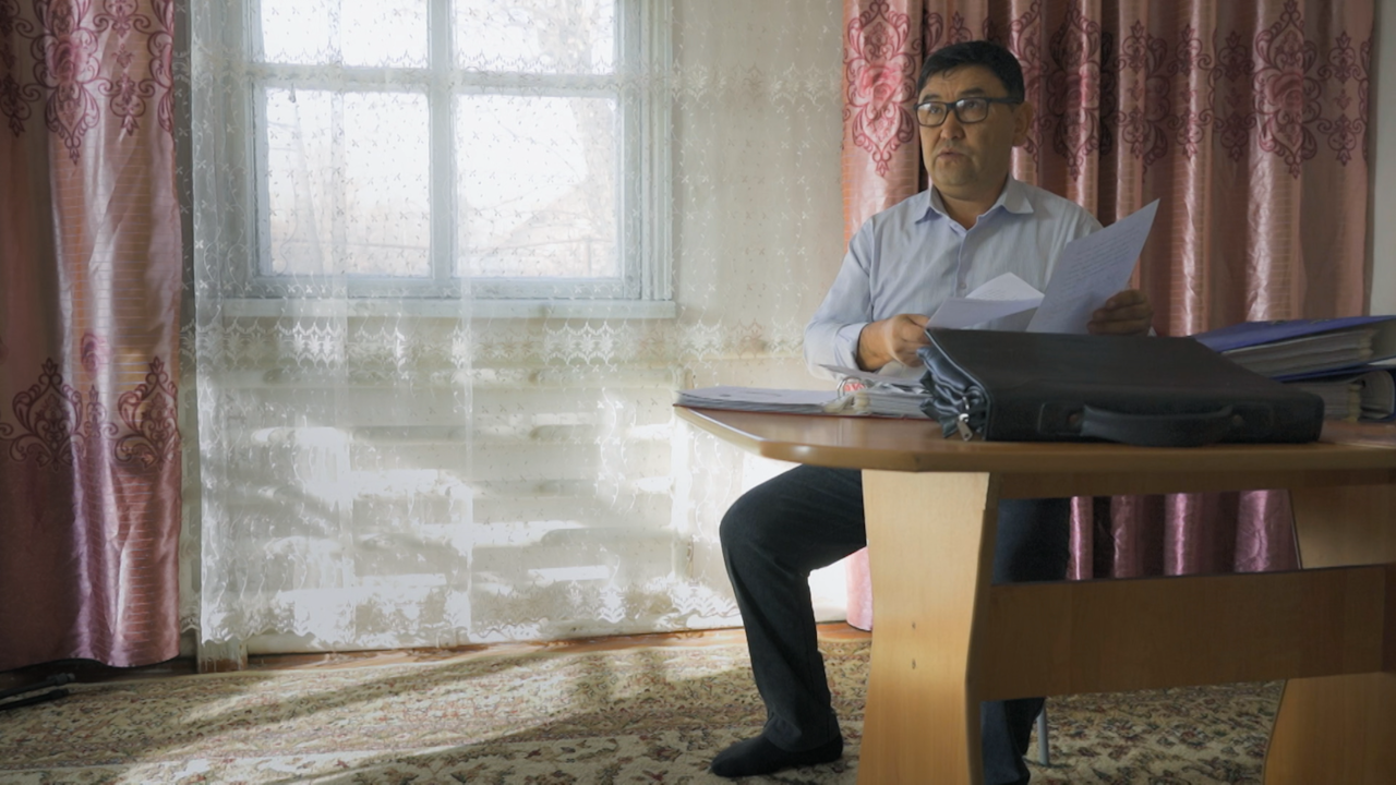 Erbol Datulbek sits at a table covered in files