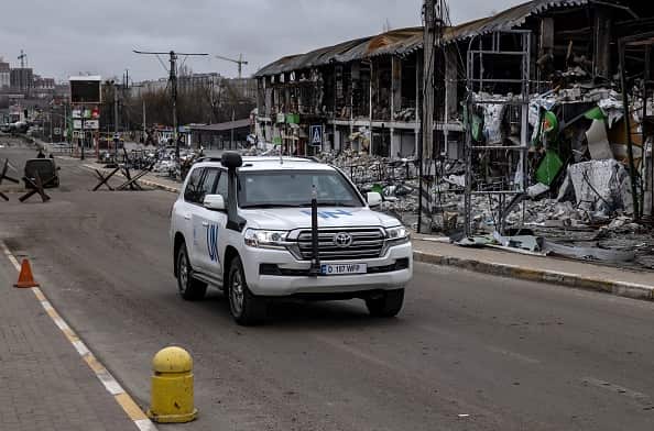 A white United Nations four wheel drive vehicle drives in front of destroyed buildings in Bucha, Ukraine.