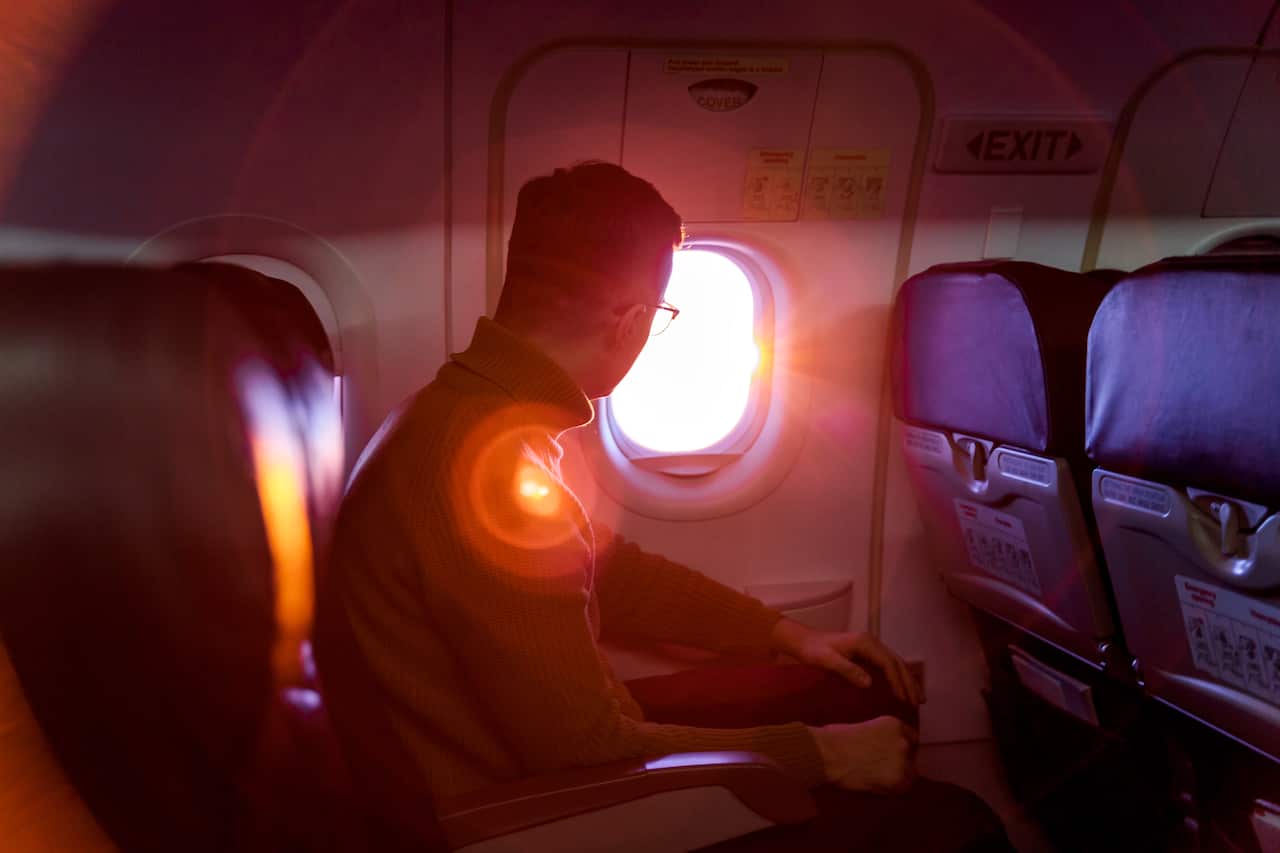Young man looking out of the window in flying airplane during sunset