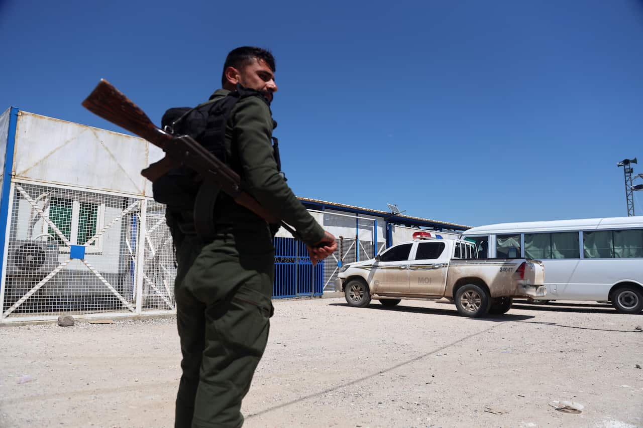 A soldier stands guard with a weapon in a carpark as vehicles arrive.