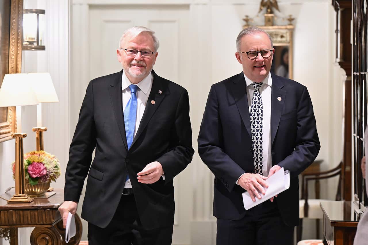 Australian Prime Minister Anthony Albanese (right) walks alongside Kevin Rudd (left) through an elegantly furnished indoor hallway. Both men are wearing dark suits and ties.