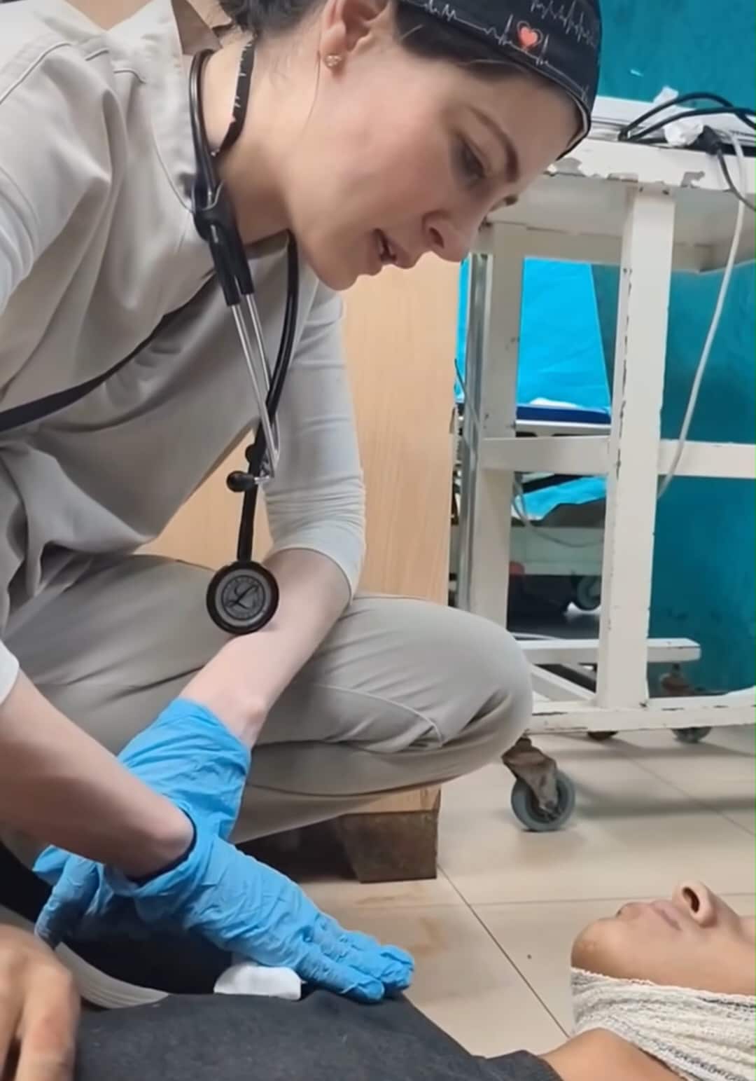 A female doctor is treating a wounded patient lying on the floor.