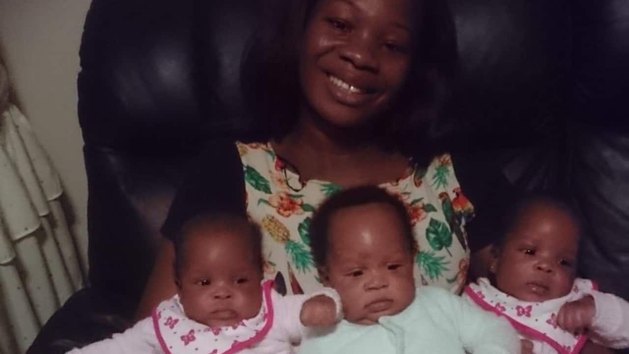 a young woman holding three young babies on her lap in an armchair
