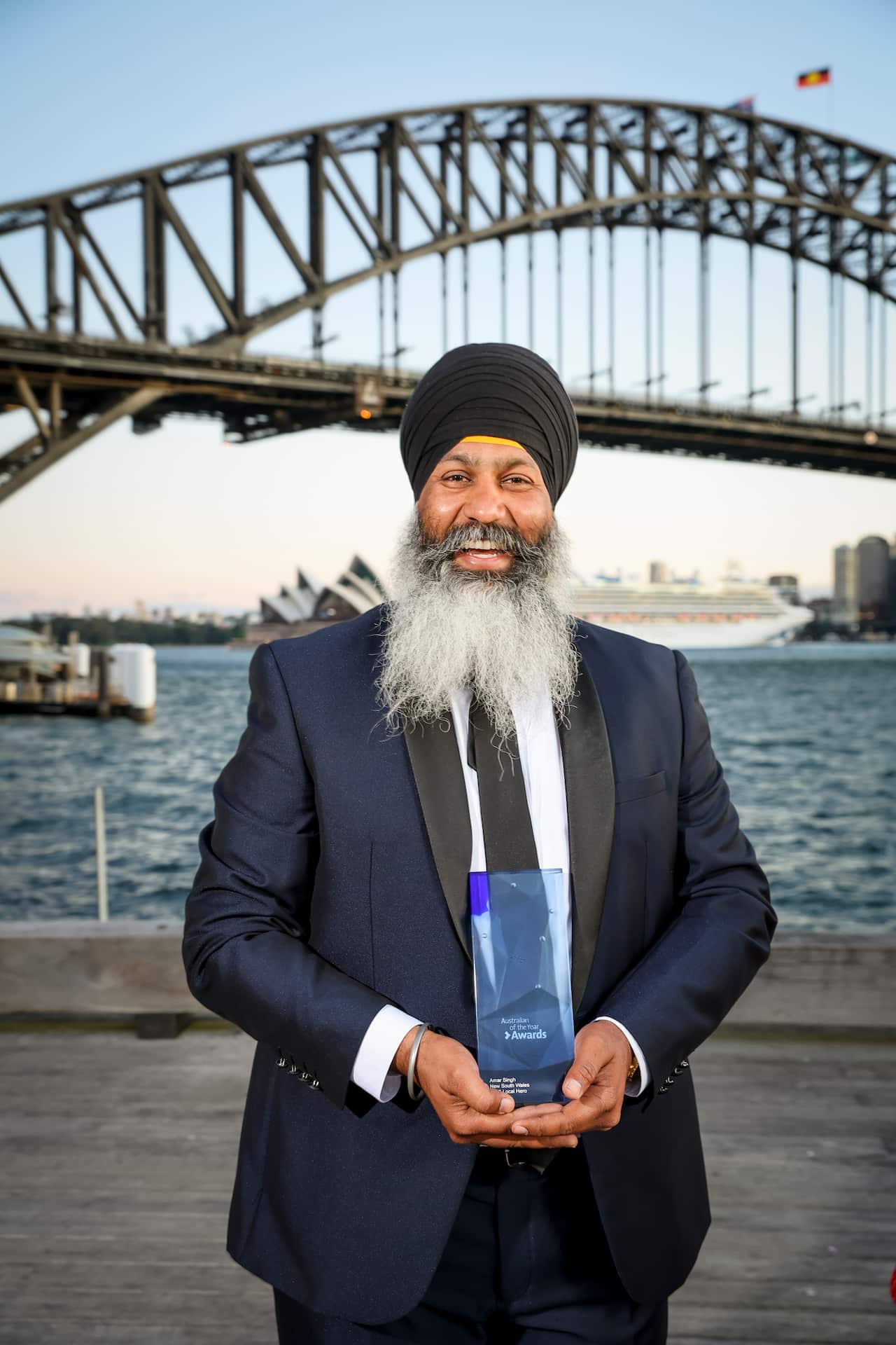 Amar Singh, founder of Turbans 4 Australia smiles while holding 2023 Australian of the Year Award. The Sydney Harbour Bridge is in the background