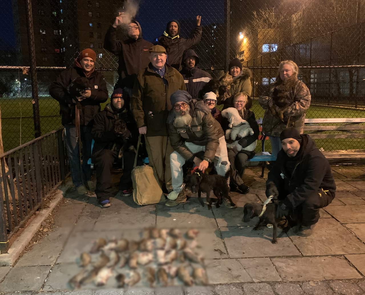 A group of twelve people poses for a photo with dozens of dead rats lying on the ground.