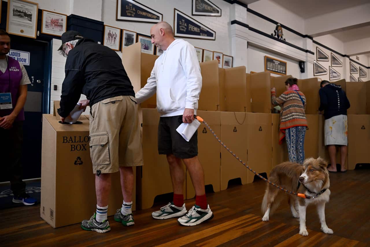 Pepole placing paper into ballot boxes, one is walking a dog.