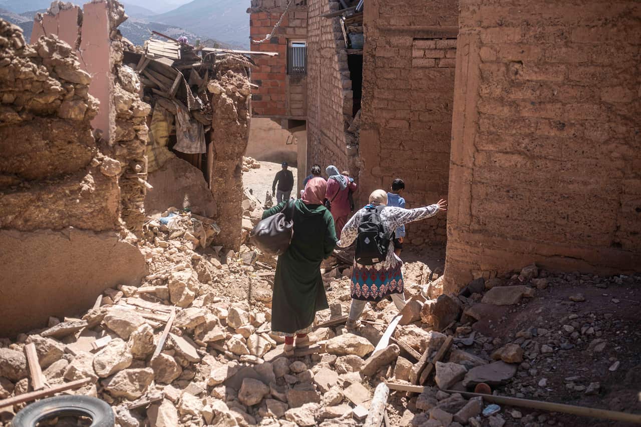 People walking through rubble surrounded by destroyed buildings.