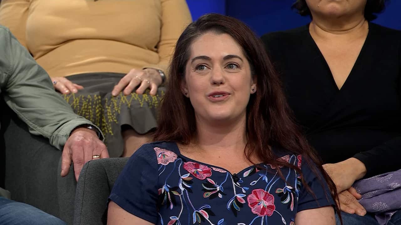 a closeup of a young woman with brown hair in a floral dress in a studio audience