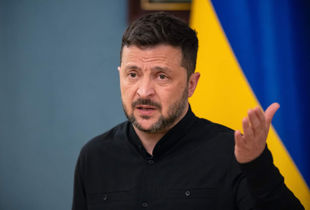 Volodymyr Zelenskyy, in a black shirt, speaks as he gestures with one hand.