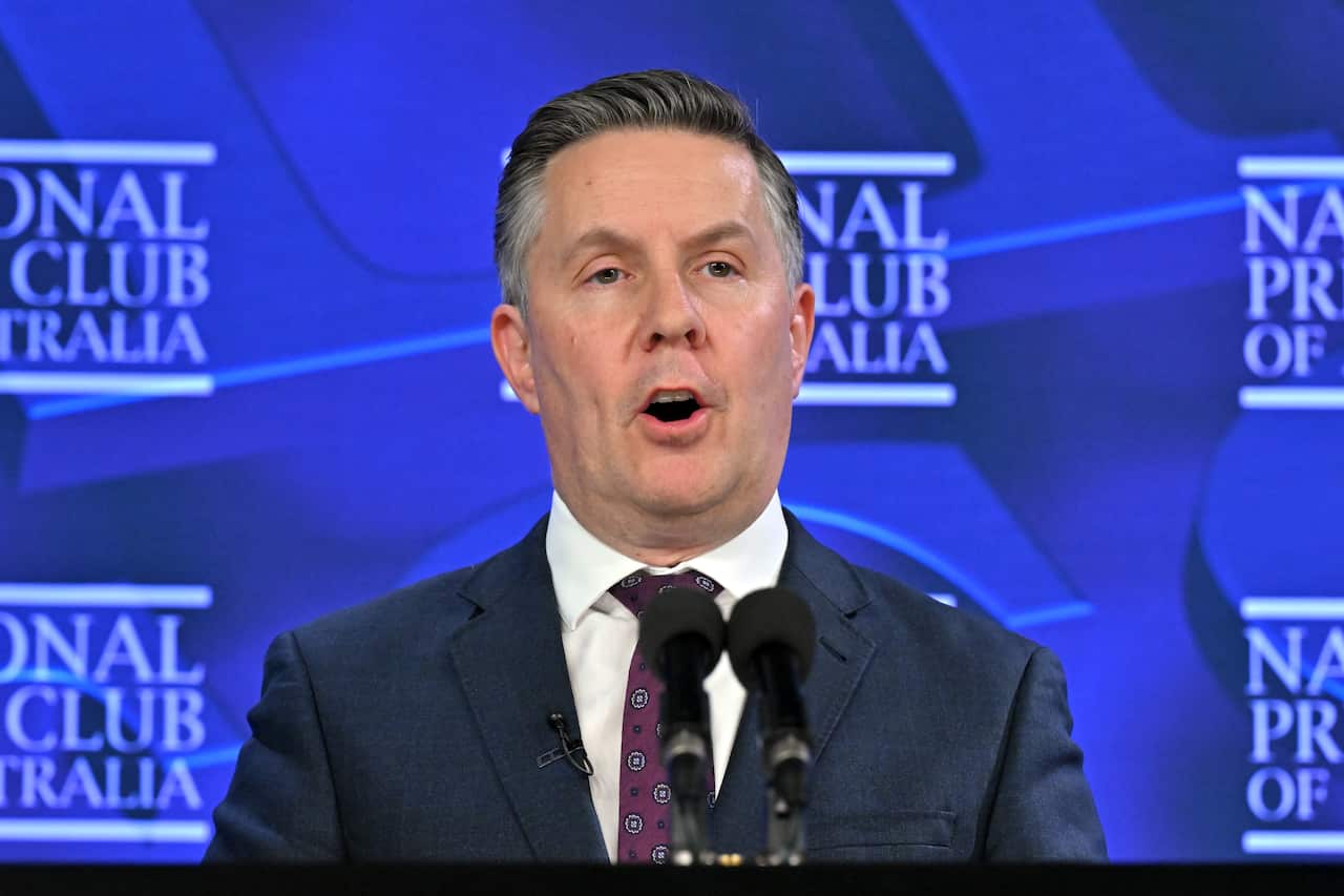  A man in a suit speaking behind two microphones in front of a blue backdrop