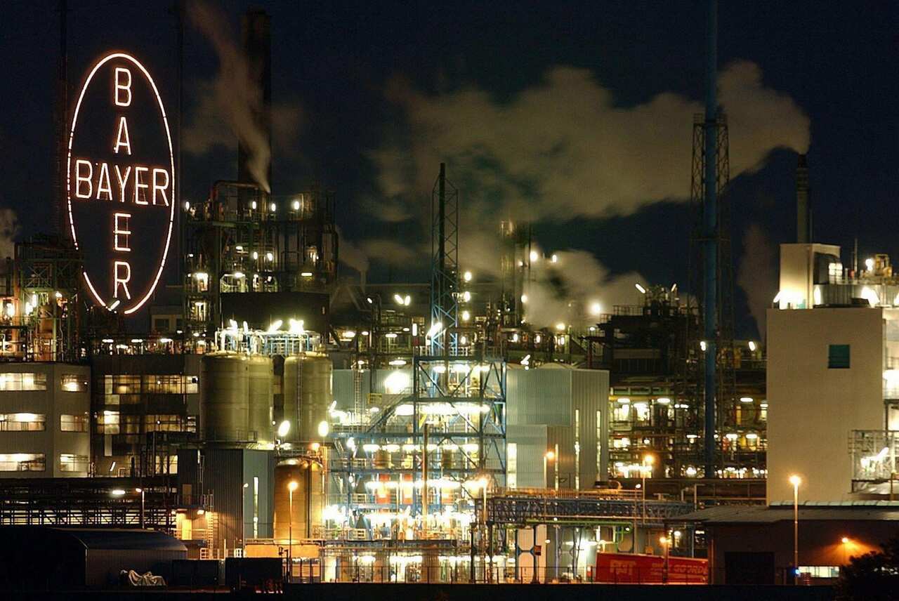 A factory at night and a neon sign that reads 'Bayer'.