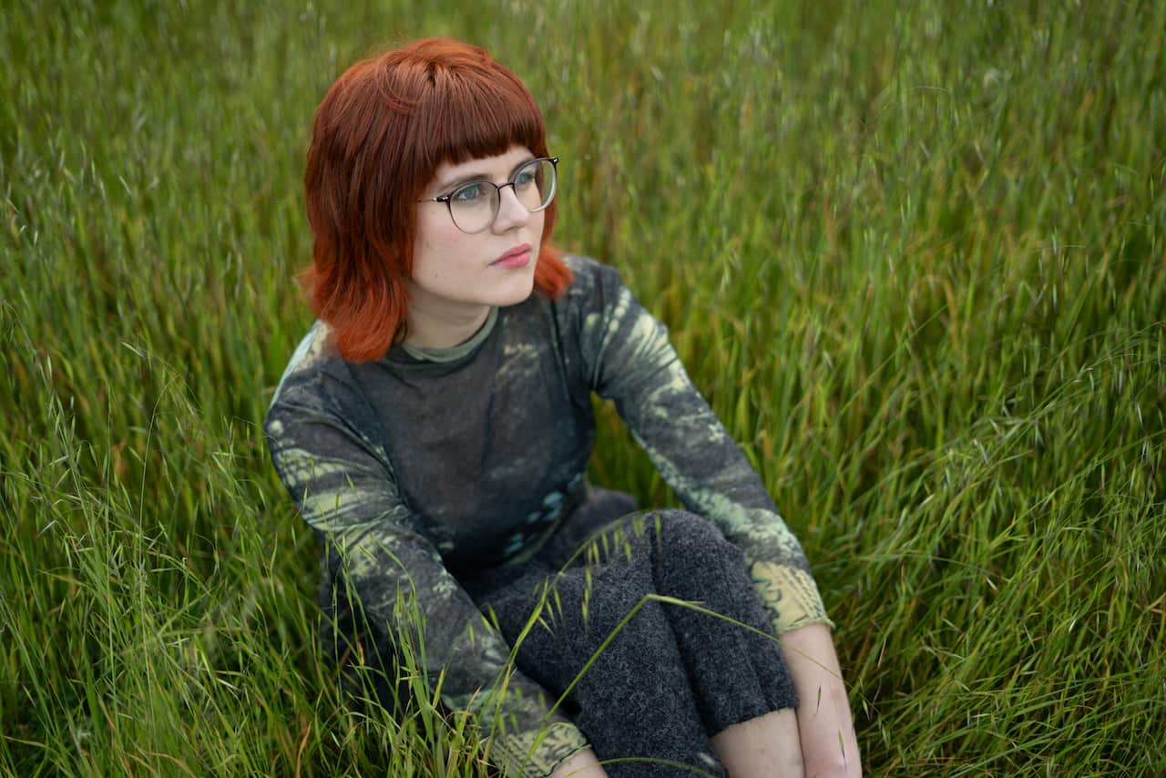 A woman sits in a field of grass. 