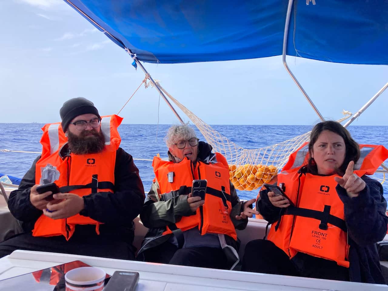 Three peopel in orange life jackets, sitting on a boat.