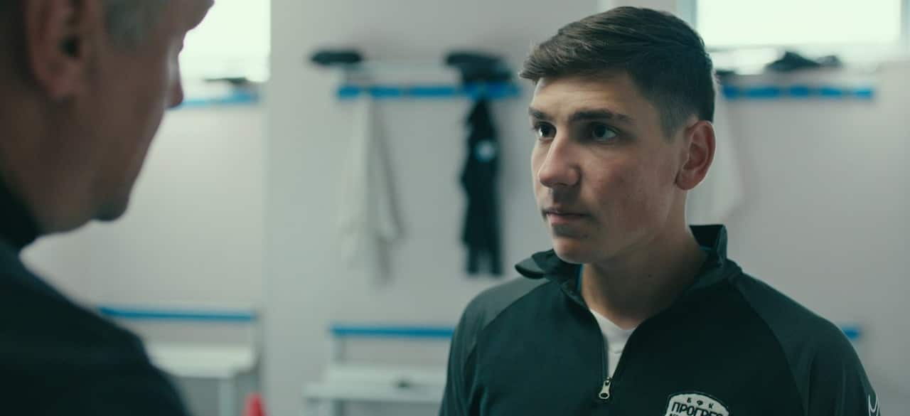 A young man stands in a sports locker room and looks a little intimidated as an older man talks to him.jpeg