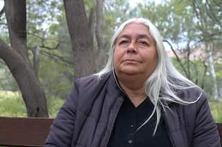 A woman with grey hair is sitting on a park bench.