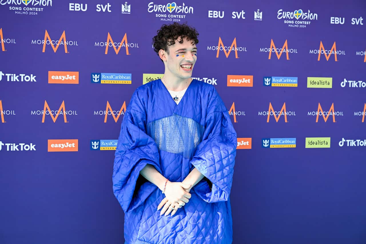 A man in a blue Japanese style dress standing in front of a purple wall with signs