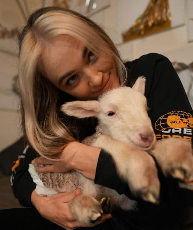 A woman with blonde hair holding a lamb 