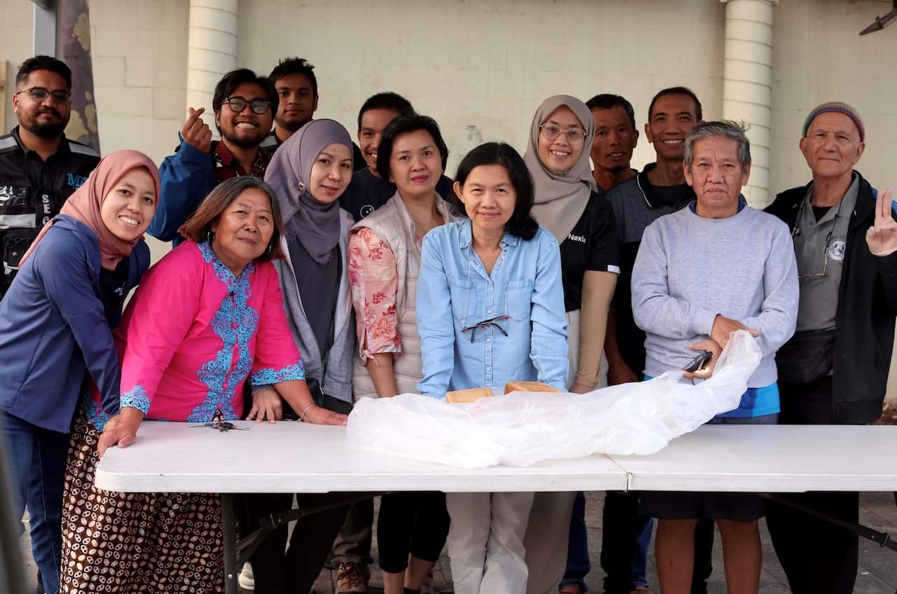 A woman in a pink jacket stands at a trestle table with a group of men and women.
