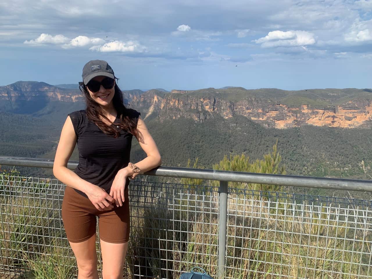 A woman in running shorts, a cap and sunglasses stands on a platform in front of mountains