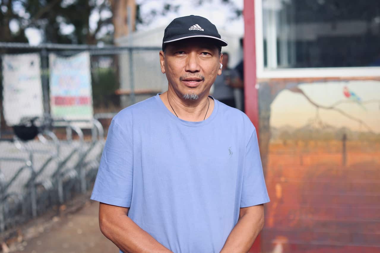 A man in a purple T-shirt and Adidas cap poses for a photo.
