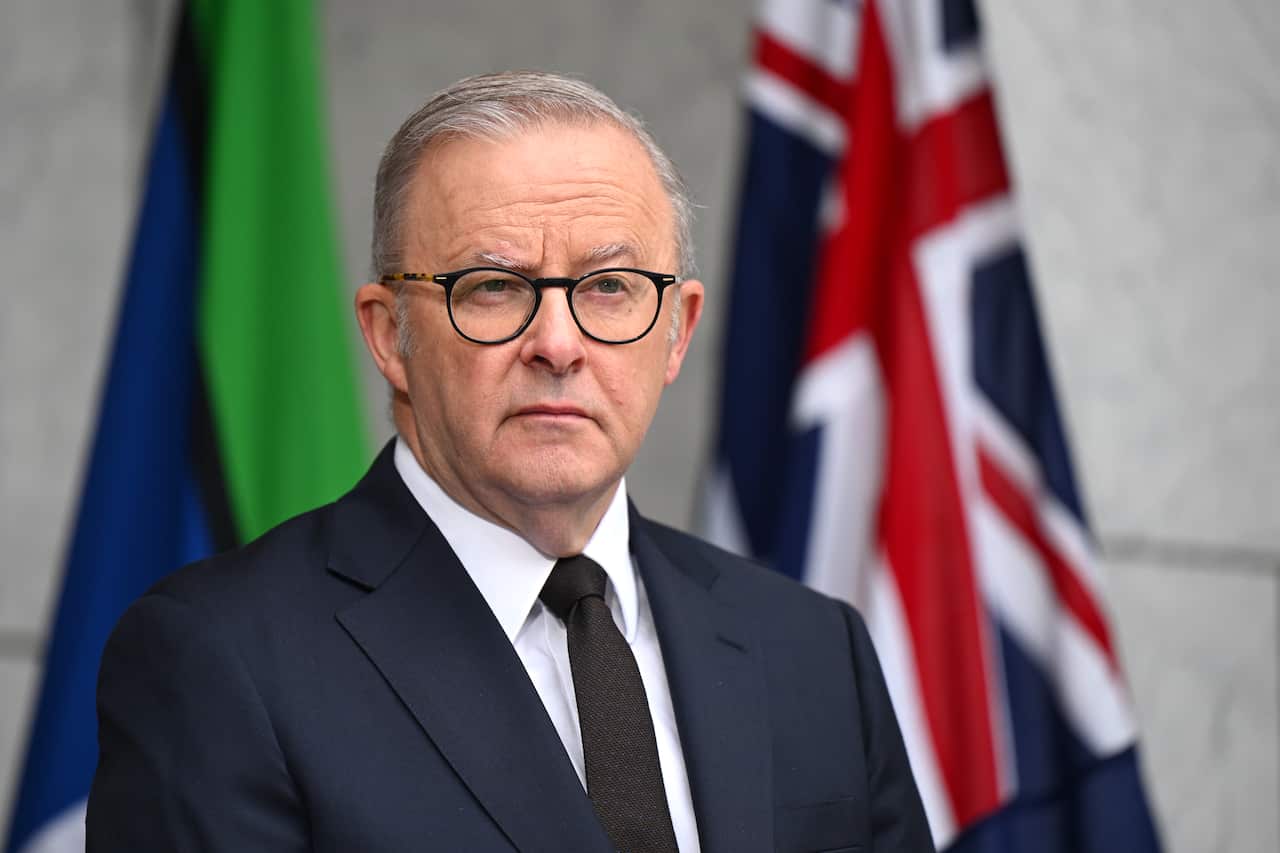 A man wearing a suit and glasses standing in front of two flags