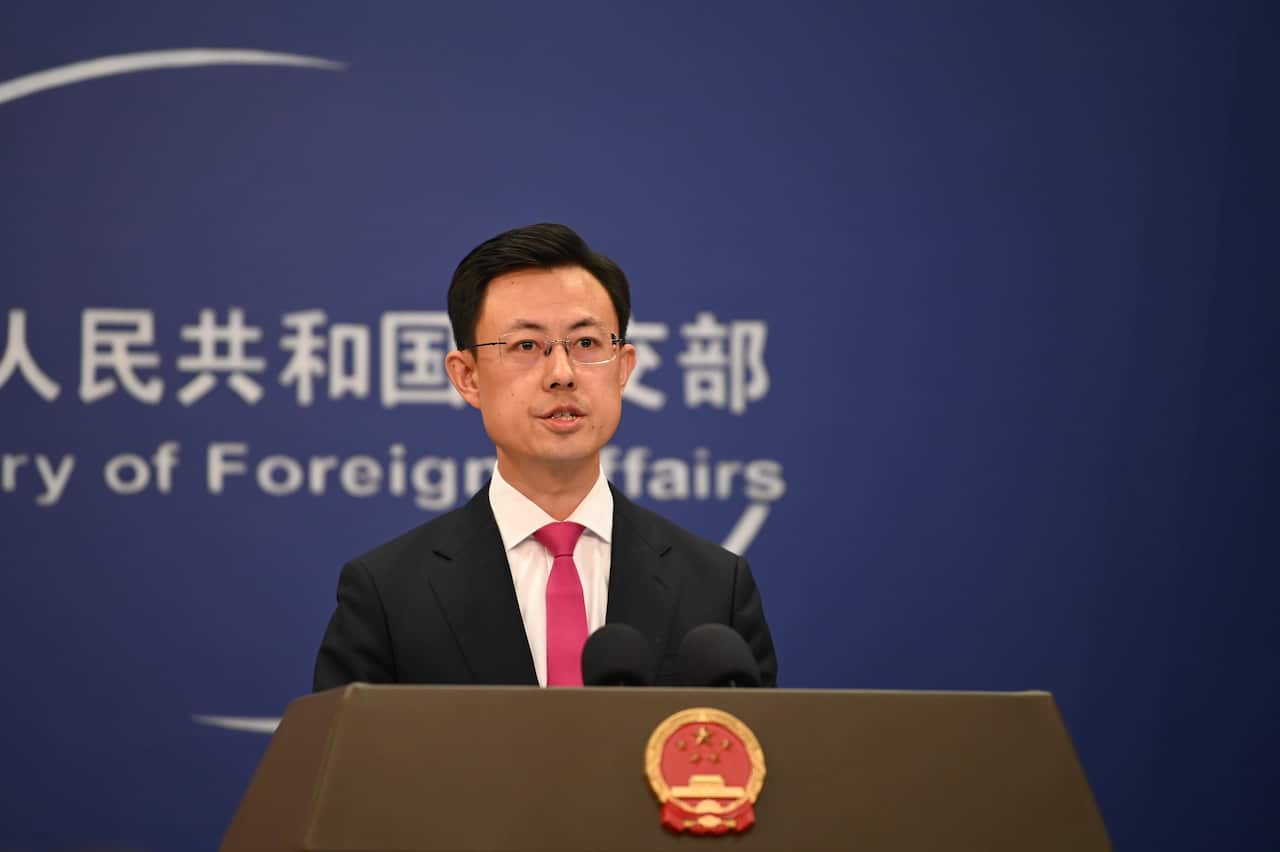 A middle-aged Asian man wearing glasses and a black suit speaking before a lectern
