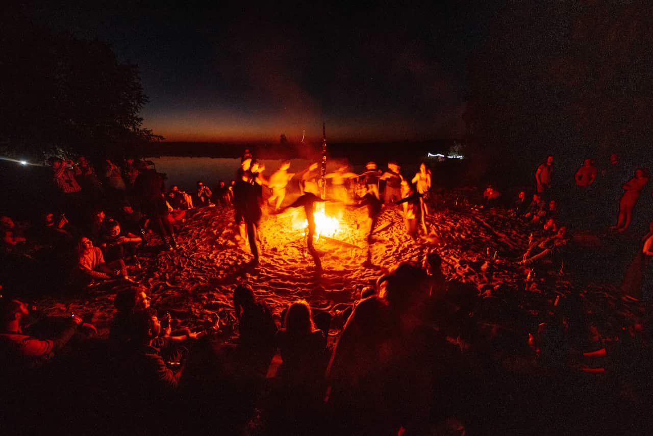 People dance and sing around a fire at night.