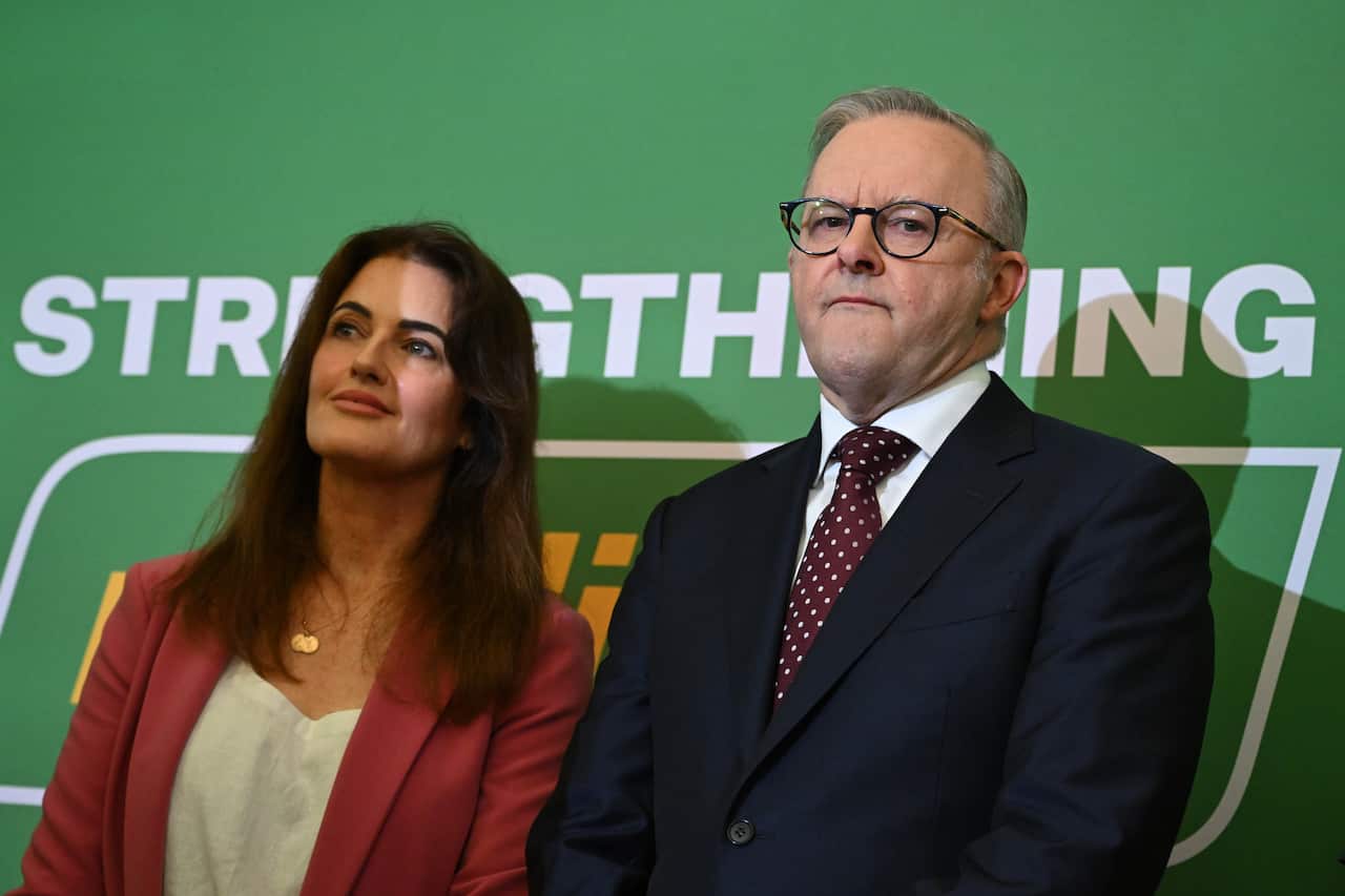 A man and woman stand in front of a green poster