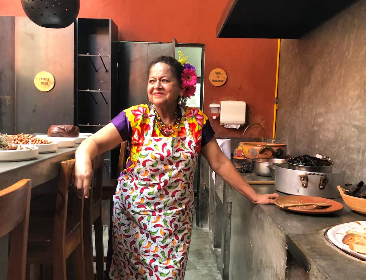 A woman in a chilli-patterned apron stands in a commercial kitchen. 