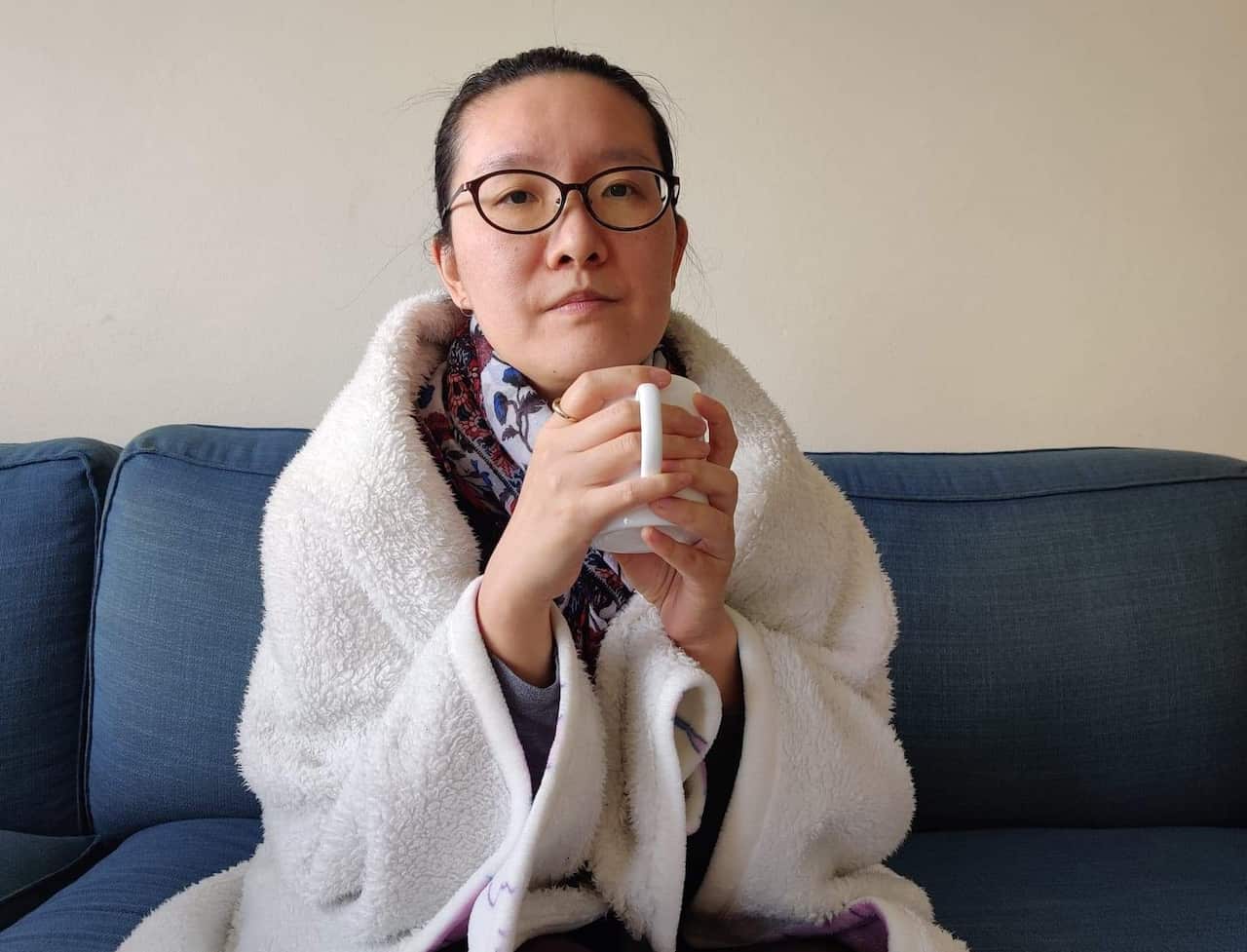 A woman with a blanket wrapped around her holding a mug.