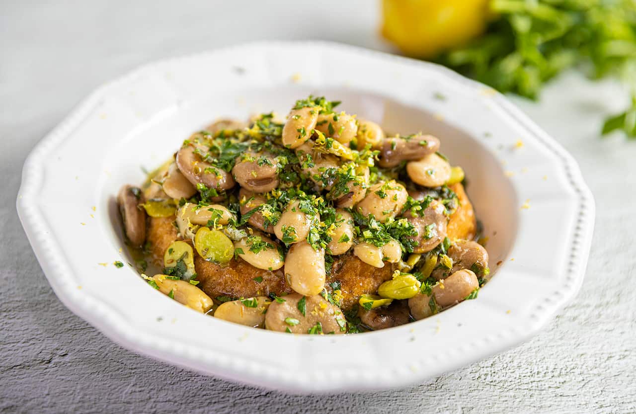 A shallow while bowl holds a barely-visible piece of bread, topped with a bean mixture.