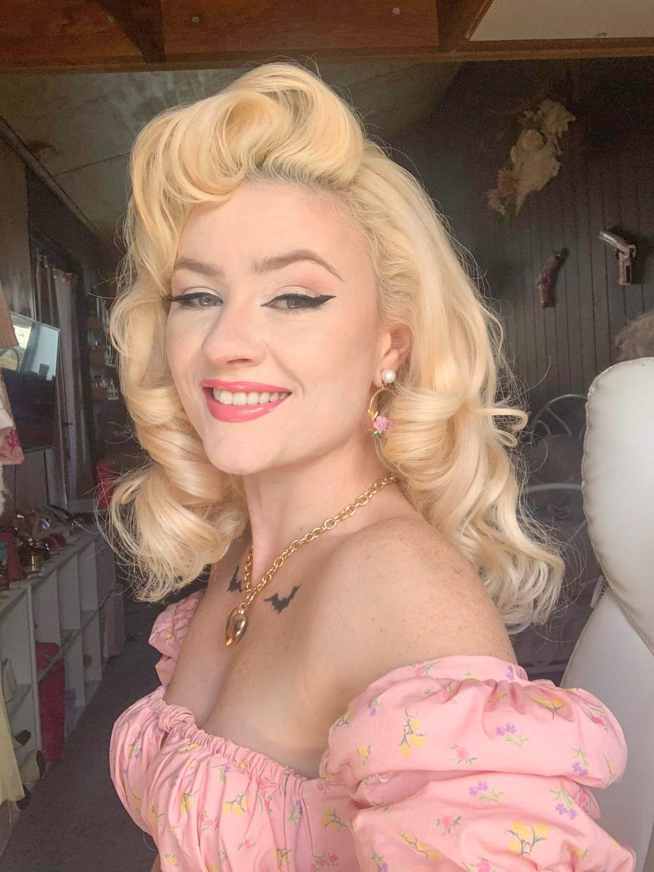 A selfie of a woman with blonde curled hair and a pink, off-the-shoulder dress.