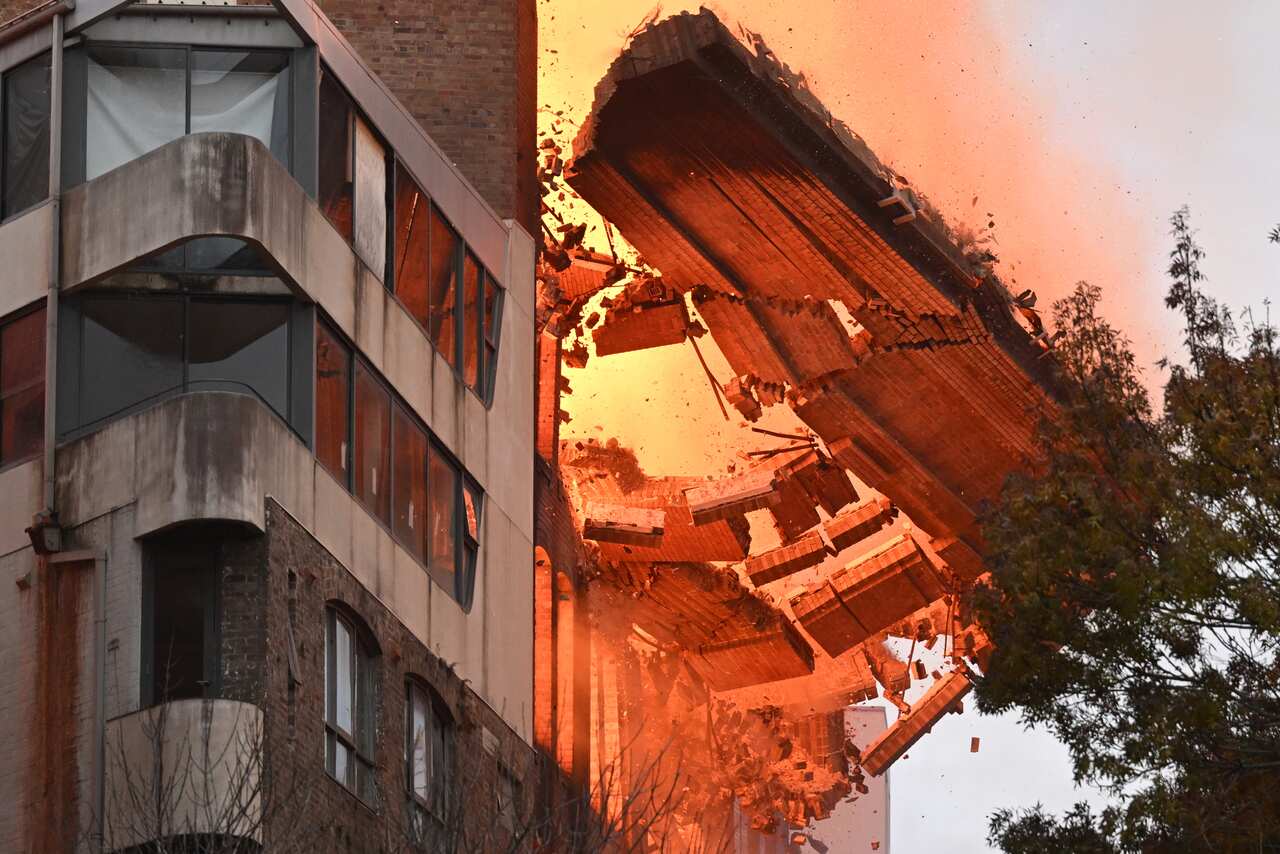 The wall of a brick building on fire collapses